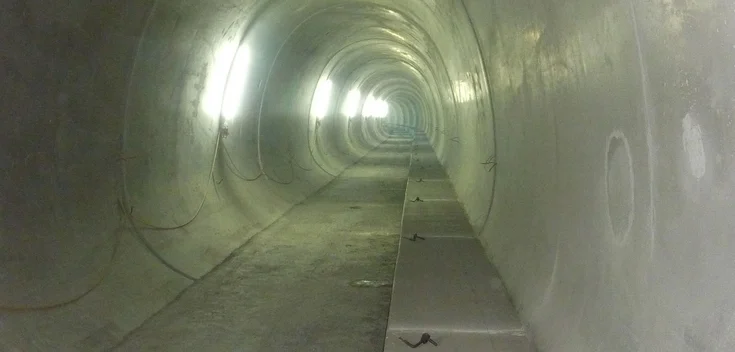 Foto: Erhöhter, aus Beton gefertigter Randweg eines Tunnels; im Hintergrund die Tunnelöffnung und Baustelleneinrichtung