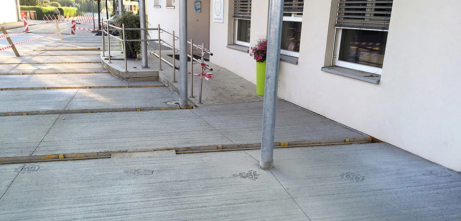 Foto: In breiten Stufen angeordnete Betonfläche vor einer Gebäudefront; eine Grünanlage im Hintergrund