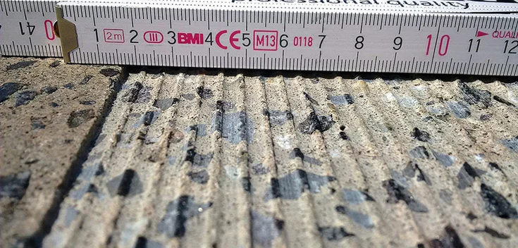 Foto: Nahaufnahme eines Bodenbelags, in den schmale Rillen geschnitten wurden; im Hintergrund ein Maßstab mit Millimeterskala