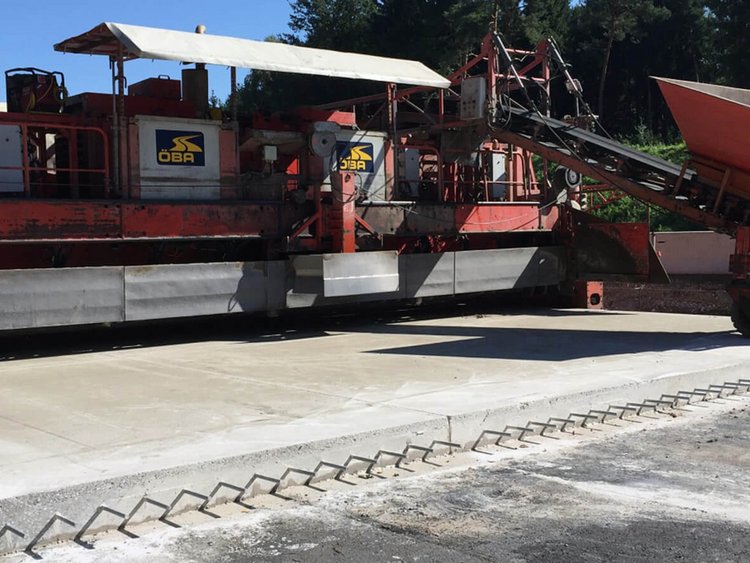 Foto: Unterbetonfertiger der ÖBA mit vorbereiteter Unterbetonplatte aus der an der Längsseite Dübel herausragen, Bäume im rechten oberen Bildteil