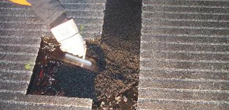 Foto: Ein Arbeiter trägt mit einer Spachtel frischen Asphalt in eine geschnittene Fuge auf.