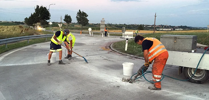 Foto: Fünf Arbeiter an einem für den Verkehr gesperrten Kreisverkehr mit diversen Werkzeugen bei der Arbeit