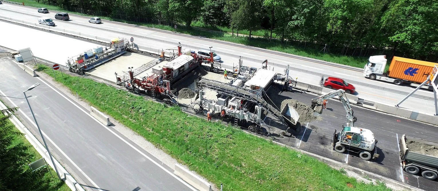 Foto: Luftaufnahme eines Betoneinbauzugs auf einer Richtungsfahrbahn; Auto- und Lkw-Verkehr auf der Gegenfahrbahn