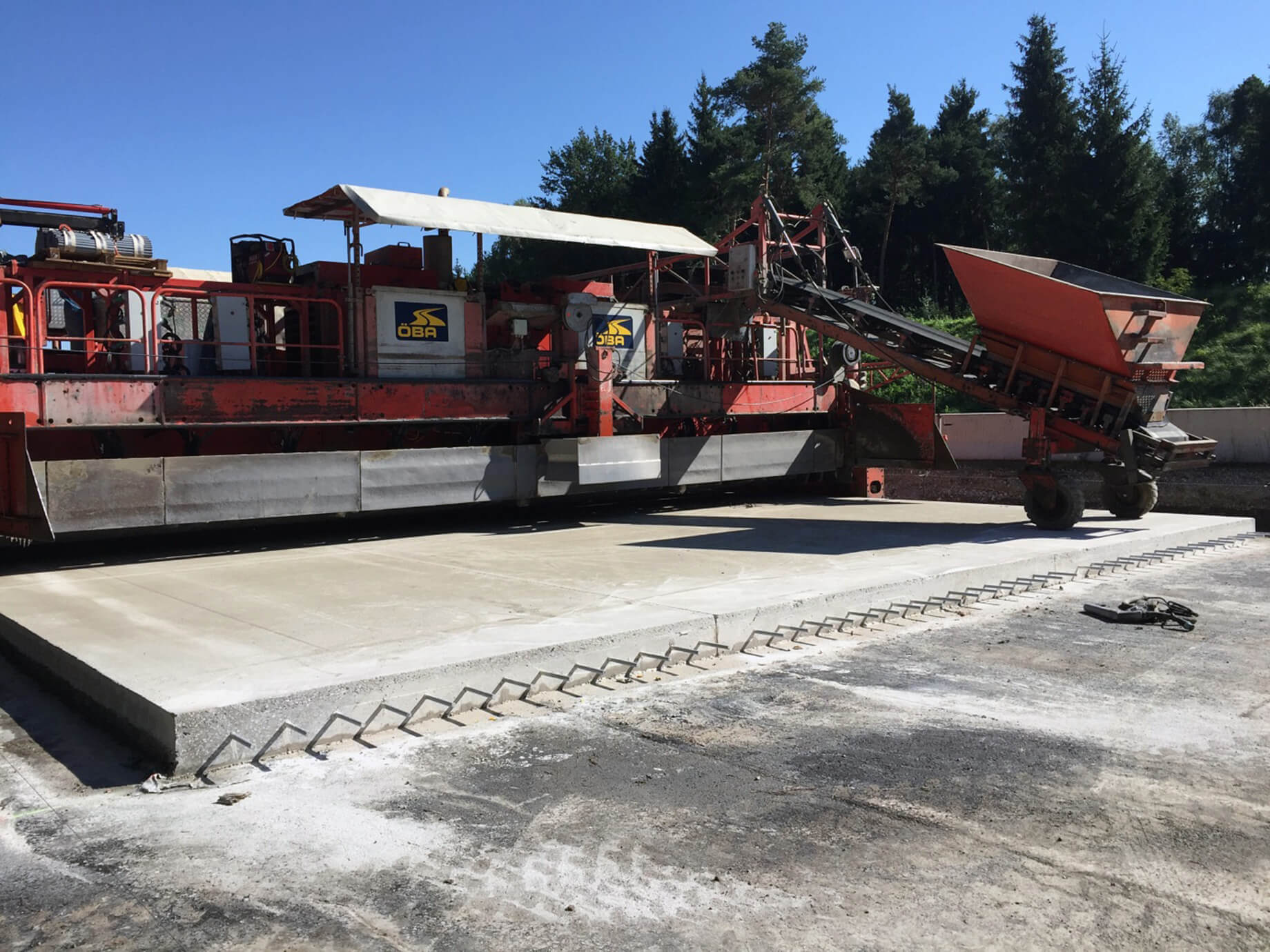 Foto: Unterbetonfertiger der ÖBA mit vorbereiteter Unterbetonplatte aus der an der Längsseite Dübel herausragen, Bäume im rechten oberen Bildteil